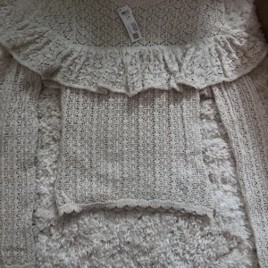 Beige spetsblus med volang - Supersöt beige blus från Lindex i spets med volangdetalj över axlarna. Blusen har lång ärm och är stickad i ett luftigt mönster. Aldrig använd prislappen är kvar 