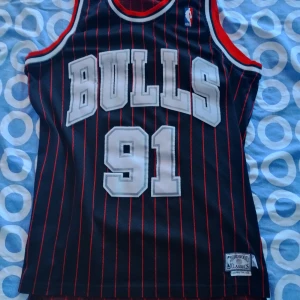 Chicago Bulls Rodman basketlinne M Retro  - Säljer ett svart Retro basketlinne från Adidas, Chicago Bulls Hardwood Classics med Rodman och nummer 91. Linnet har röda och vita detaljer, tunna röda ränder och stora tryckta siffror och bokstäver fram och bak. Perfekt för basketfans som vill sticka ut.