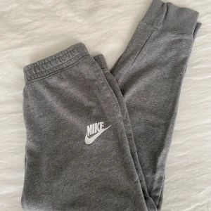 Grå mjukisbyxor från Nike, storlek L - Använda 1 gång. Grå mjukisbyxor från Nike med klassisk vit logga på benet. Byxorna har resår i midjan och är gjorda i mjukt bomullsmaterial, perfekta för chill eller träning. Snygg och enkel design som passar till sneakers och hoodie.