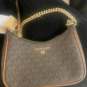 Michael Kors brun handväska med kedja - Helt oanvänd Michael Kors väska, köpt från Zalando. Prislapp kvar. Kan tänka mig gå ner lite vid snabb affär. 