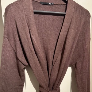 Brun stickad kofta med knytband  - En väldigt fin brun stickad kofta med band från lager 157. Den har ett väldigt skönt material som inte sticks och värmer väldigt bra, passar därför perfekt nu till vintern. Den har använts endast 1 gång och jag säljer den pga att armarna är för långa. Den är i mycket bra skick och har inga defekter. Rekommenderar starkt!🤍 Vid frågor så är det bara och höra av sig, pris kan även diskuteras🫶