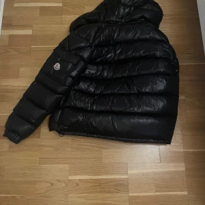 Svart pufferjacka från Moncler maya  - Mayapufferjacka från Moncler med dragkedja och huva. Jackan har långa ärmar och praktiska fickor med dragkedjor. Perfekt för kyliga dagar. 📫Kvitto finns 🧾🧾