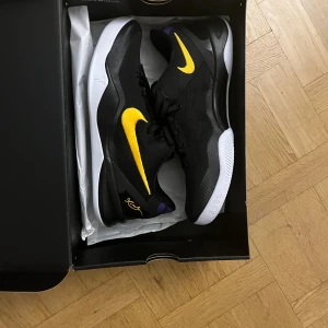 Kobe 8 protro lakers away - Grymma Nike Kobe sneakers i svart mesh med gul Swoosh och signaturdetalj på hälen. Snygga kontraster med vit platt sula och inslag av lila. Skorna har snörning och rund tå, perfekt för dig som gillar basketstil och sportig vibe.