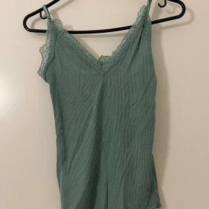 2 ribbade linnetoppar med spets - Säljer två ribbade linnetoppar från SUI, en i ljusgrön och en i beige. Båda har smala axelband, v-ringning och spetsdetaljer längs urringningen. Perfekta att styla lager på lager eller till jeans. Mjukt och stretchigt material för en bekväm känsla.