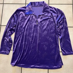 Lila sammets pikétröja med fjädermönster storlek M/L - Unik lila pikétröja i glansig sammet med subtilt fjädermönster. Tröjan har klassisk krage, två knappar framtill och långa ärmar. Perfekt för dig som vill sticka ut med en cool vintage vibe och mjuk känsla.