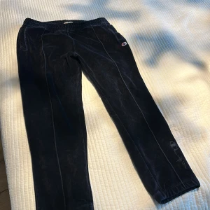 Svarta mjukisbyxor från Champion - Svarta mjukisbyxor från Champion i mjuk sammet med elastisk midja och sidofickor. Byxorna har broderad Champion-logga på benet och en liten logga vid fickan. Perfekta för en chill och avslappnad stil.