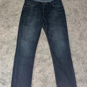 Mörkblå Lee jeans straight fit  - Snygga mörkblå jeans från Lee med klassisk femficksdesign och brunt Lee-läderpatch bak. Jeansen har raka ben och subtila slitningar framtill för en cool look. Passar dig som gillar tidlös stil och vill ha ett par jeans som funkar till allt.