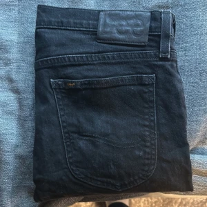 Svarta skinny jeans från Lee - Svarta jeans från Lee med klassisk femficksdesign och skinny passform. Jeansen har dragkedja och knapp framtill, samt Lee-logga på bakfickan och läderpatch i midjan. Materialet är mjukt denim som sitter snyggt och bekvämt.