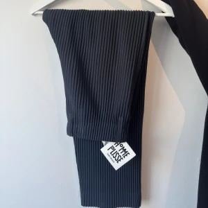 Svarta plisserade byxor Homme Plissé - Mörk gråa plisserade byxor från Homme Plissé Issey Miyake med elastisk midja och raka ben. Byxorna har en snygg ribbad struktur och är tillverkade i ett lätt material som även ger en riktigt snygg siluette . Perfekta för dig som gillar stilrena och unika plagg. Helt nya och endast använda för att ta annonsbilderna! Nypris är 2995kr, men säljer för 1990kr!  