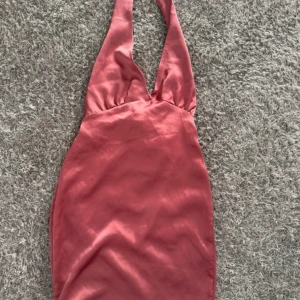 Rosa omlottklänning från PrettyLittleThing - Snygg kort rosa klänning i satin från PrettyLittleThing. Klänningen har omlott-design med breda axelband, djup v-ringning och knyt i ryggen för en cool siluett. Materialet är glansigt och mjukt, perfekt för att sticka ut. Passformen är tight och figurnära.