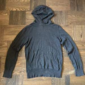 Mörkgrå hoodie i stickad bomull S - Mörkgrå hoodie i stickad bomull med klassisk huva och känguruficka framtill. Tröjan har ribbade muddar vid ärmslut och nederkant samt lång ärm. Perfekt för en chill och avslappnad stil.