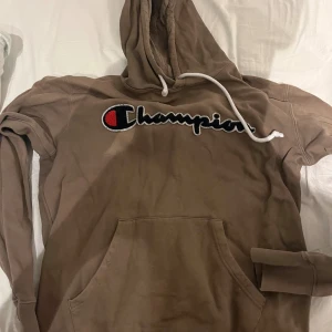 Brun Champion hoodie med broderad logga - Säljer en brun hoodie från Champion i storlek medium. Tröjan har stor broderad Champion-logga på bröstet, vit snörning i huvan och en klassisk magficka. Mjuk bomullsmix och långärmad modell, perfekt för chill dagar. Passar S och M