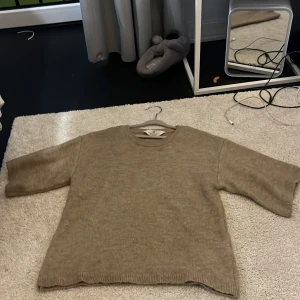 Beige stickad tröja från H&M - En beige stickad tröja från H&M med rund hals och trekvartsärmar. Tröjan har en loose passform och är tillverkad i mjukt stickat material som ger en chill och avslappnad vibe. Perfekt för lager-på-lager under hösten och vintern.
