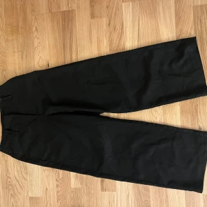 Svarta kostymbyxor från Amisu - Svarta kostymbyxor från Amisu i storlek 32. Byxorna har raka, vida ben och hög midja med hällor för bälte. Snygg och stilren modell som passar perfekt till vardag eller när du vill klä upp dig lite. Lite noppriga (se bild)