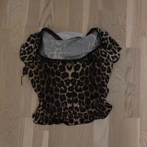 Leopardmönstrad blus med volang - Säljer en leopardmönstrad blus med korta puffärmar och volangkant. Toppen har en rundad hals med svart spetsdetalj och är gjord i ett lätt, transparent syntetmaterial. Perfekt för dig som vill sticka ut med ett djuriskt mönster. Köpt här på plick. Köptes för 150. Måste verkligen bli av med kläder så lägg gärna ett prisförslag om ni är intresserade, är öppen för alla rimliga priser💗💗 