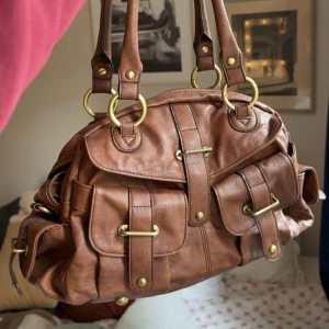 Brun axelväska - Köper ni innan 19 postar jag samma dag💓Snygg brun axelväska med flera fickor och coola guldfärgade spännen. Har aldrig använt den då jag har flera väskor jag måste bli av med💓 (kolla min profil för flera plagg!) Perfekt för dig som vill ha en rymlig och stilren väska med detaljer som sticker ut. 🤩🤩