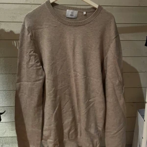 Beige stickad tröja från Black - En enkel och stilren beige stickad tröja från Black. Tröjan har rund halsringning och långa ärmar, perfekt för lager-på-lager. Materialet är mjukt och skönt mot huden, och den neutrala färgen gör den lätt att matcha med allt.