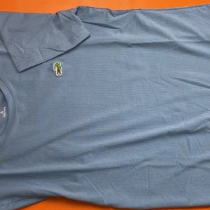 Blå t-shirt med broderad patch - Snygg blå t-shirt i mjuk bomull med en liten broderad patch på bröstet som föreställer Lacoste. Klassisk rund halsringning och korta ärmar. Perfekt för en chill och avslappnad stil.