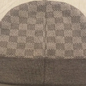  grå mössa - Snygg mössa i grått och beige med klassiskt rutigt mönster. Mössan har en uppvikt kant med logga framtill och är stickad i mjukt material som känns lyxigt. Perfekt för dig som vill ha en stilren accessoar med designer-vibe.