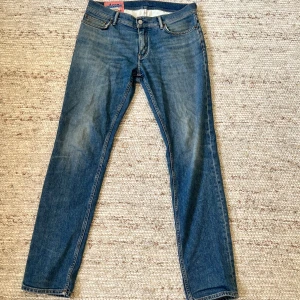 Acne Blå Konst blå jeans 32/30 - Snygga blå jeans från Acne Blå Konst med klassisk femficksdesign och raka ben. Jeansen har normal midja och subtila slitningar för en cool look. Tillverkade i bomull för skön passform och stilren känsla. 32/30 men passar mer 32/32 tidigare ägare har tagit bort lappen på utsidan om någon undrar
