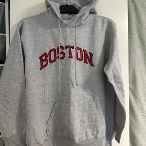 Vintage Boston hoodie - Grå vintage hoodie med rött och svart BOSTON-tryck på bröstet. Ficka framtill och luva. Köpt i USA cirka år 2010, mycket bra skick fortfarande. Enda skavanken är ett litet grönt streck av krita på baksida axel (se sista bild)  