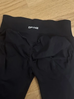 Dfyne impact leggings  - Säljer ett par svarta leggings från DFYNE impact leggings i storlek medium. Texten är lite sliten vilket syns på bilden. Leggingsen är helt slutsålda.  Färgen heter midnight black. De har hög midja och är tillverkade i ett stretchigt material med 90% nylon och 10% elastan. Perfekta för träning eller chill, med snygg logga framtill på linningen.