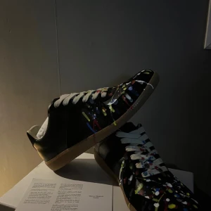 Maison Margiela gats med färgstänk - Svarta sneakers från Maison Margiela i skinn med unika färgstänk i blått, rött, gult och vitt. Skorna har vita snören och en klassisk gummisula i beige. Skriv för frågor på skorna! De används medan de är ute men väldigt sparsamt 😁 skriv vid bilder eller funderingar☺️