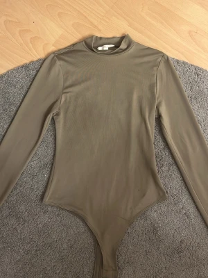 Långärmad bodysuit från H&M XS - Säljer en tight och stretchig beige bodysuit från H&M i storlek XS. Den har lång ärm, hög hals och är gjord i ett mjukt, tunt material som sitter riktigt snyggt på kroppen. Perfekt att styla med jeans eller kjol.