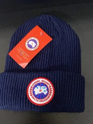 Mörkblå stickad mössa  - Säljer en mörkblå ribbstickad mössa med klassisk rund logotyp framtill. Mössan är i ett mjukt och varmt material, perfekt för kyliga dagar. Snygg och enkel design som passar till det mesta.