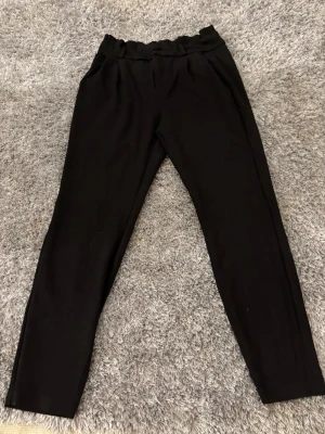 Svarta högmidjade kostymbyxor - Snygga svarta kostymbyxor med hög midja och rynkad linning. Byxorna har raka ben och praktiska fickor fram. Materialet känns mjukt och har en lätt stretch, perfekt för en chill och stilren look. Fickorna där bak är ej öppningsbara!💕