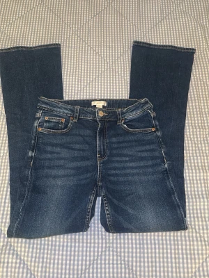 Blå bootcut jeans från Gina Tricot - Snygga blå jeans från Gina Tricot med klassisk femficksdesign och bootcut-ben. Jeansen har normal midja och är gjorda i mjukt bomullsmaterial med lite stretch för extra komfort. Perfekt passform och cool tvätt med lätt slitning framtill.