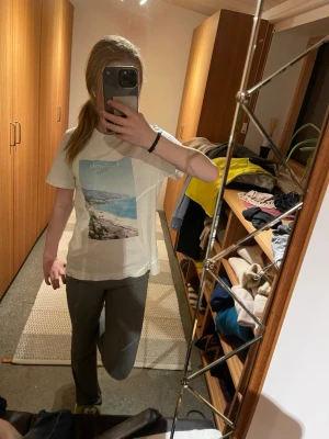 Vit t-shirt med strandmotiv - Säljer en vit t-shirt med ett stort tryck av ett strandmotiv och texten 'California' på bröstet. T-shirten har korta ärmar och en klassisk passform. Perfekt för dig som gillar chill och enkel stil.