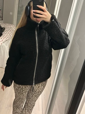 Svart teddyjacka med dragkedja - Mysig svart teddyjacka med hög krage och grov dragkedja framtill. Jackan har en loose passform och är tillverkad i fluffigt fleece-material som håller dig varm. Perfekt för dig som gillar en chill och trendig look under höst och vinter. Passar xs-M jag är 170