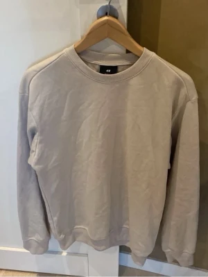 Beige sweatshirt - Säljer en enkel och stilren beige sweatshirt från H&M. Tröjan har rund hals, ribbade muddar vid ärmslut och nederkant samt lång ärm. Perfekt för dig som gillar en clean look och vill ha något mjukt och bekvämt i garderoben. Pris hugget i sten