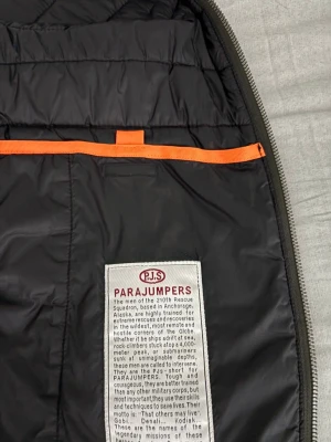 Svart dunväst från Parajumpers  - Säljer en svart dunväst från Parajumpers i storlek L. Västen har quiltad design, dragkedja framtill och coola orange detaljer. Perfekt för lager-på-lager och funkar till många olika stilar. Märket syns tydligt på både insidan och utsidan.