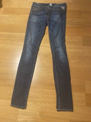 Replay Luz skinny jeans blå - Snygga Replay Luz skinny jeans i mörkblå tvätt med coola slitningar och klassiska detaljer. Modellen har låg midja, smal passform och fem fickor. Materialet är stretchigt jeans för en bekväm känsla. Perfekt för dig som gillar en tajt siluett och streetstil.
