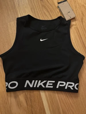 Svart Nike Pro sport-topp XS - Nike Pro sport topp i svart med vit logga framtill och bred resår med 'NIKE PRO' i vitt. Tillverkad i Dri-FIT material som andas och håller dig torr under träning. Helt oanvänd med prislapp kvar!!