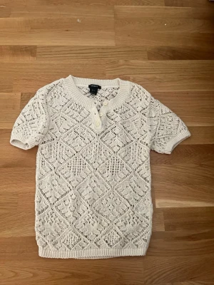 Vit stickad kortärmad tröja Lindex - Säljer en vit stickad tröja från Lindex i storlek S. Tröjan har korta ärmar, rund halsringning och snygga knappar framtill. 