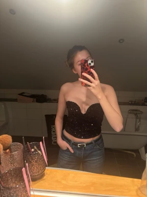 Svart paljett korsett-topp - Säljer en svart croppad korsett-topp täckt av glittriga paljetter. Toppen är axelbandslös med en snygg sweetheart-urringning och sitter tight runt kroppen. 