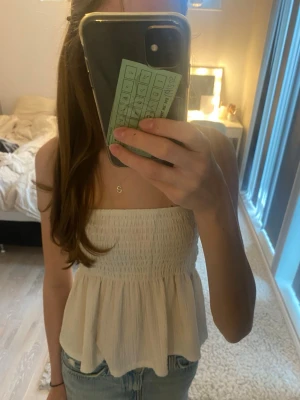 Vit bandeau tubtopp från Gina Tricot - Säljer en vit bandeau tubtopp från Gina Tricot i storlek XS. Toppen har smockad överdel och ett volangformat fall nedtill. Materialet är mjukt och lätt, perfekt för varma dagar. Enkel och stilren design som är lätt att matcha med jeans eller kjol. 