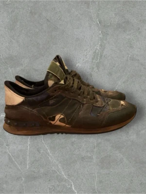 Valentino Rockrunner - Säljer ett par Valentino Rockrunner sneakers med coolt camouflage-mönster i grönt, beige och svart. Skorna har snörning, platt sula och detaljer i skinn och mocka. Perfekta för dig som vill sticka ut med ett lyxigt streetwear vibe.