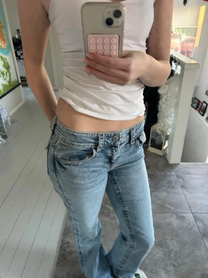 Lågmidjade ljusblå bootcut jeans - Säljer ett par riktigt snygga lågmidjade jeans i ljusblå tvätt med bootcut passform. Jeansen har klassiska fickor fram och bak, samt coola sömdetaljer och knappstängning. Perfekta för dig som gillar en avslappnad och trendig look.