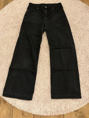 Svarta wide jeans från Monki - Säljer ett par svarta jeans från Monki med breda ben och klassisk femficksdesign. Jeansen har hög midja och raka, loose passform. Materialet är robust denim i bomull och de har knapp och dragkedja framtill. Perfekt för dig som gillar en avslappnad stil.