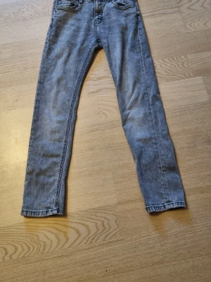 Grå skinny jeans från kappahl - Säljer ett par grå skinny jeans från kappahl  med klassisk femficksdesign och dragtjedjegylf. Jeansen har en smal passform och är tillverkade i mjukt denimtyg som sitter snyggt på benen. Perfekt för dig som gillar en stilren och enkel look.