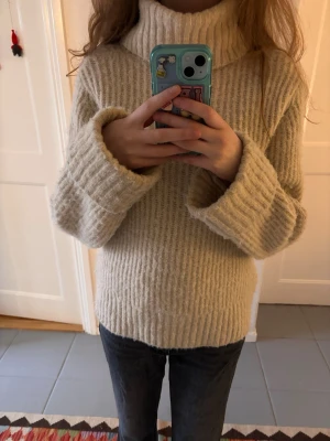 Beige ribbad polotröja stickad - Mysig beige polotröja med bred ribbstickning och lång ärm. Tröjan har en hög och bred polokrage som ger extra värme och en chill vibe. Passformen är loose och materialet känns mjukt och stickat, perfekt för kalla dagar.