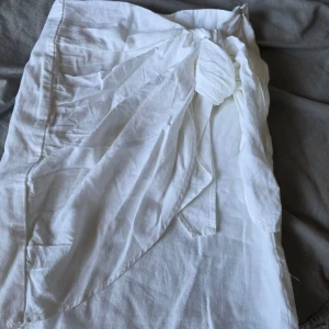 Vit omlottkjol från BikBok i linne - Snygg vit omlottkjol från BikBok i luftig linnemix. Kjolen har knytband i midjan och en lätt volangig känsla framtill. Perfekt för varma dagar och enkel att styla med crop tops eller t-shirts.