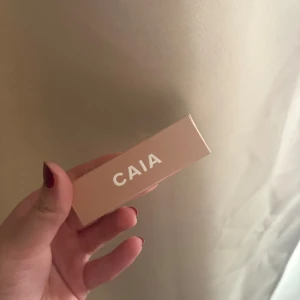 CAIA Glossy Lipstick 90's Vibe - Säljer ett CAIA Glossy Lipstick i färgen 90's Vibe. Det är ett krämigt läppstift med glansig finish i en snygg nude-beige ton. Kommer i en stilren, ljusrosa hylsa med silverdetaljer. Perfekt för dig som gillar en naturlig look med extra glow.