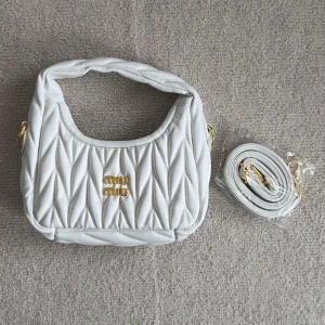 Vit quiltad handväska från Miu - Supersnygg vit handväska från Miu Miu med quiltad design och guldfärgade detaljer. Väskan har ett kort handtag och en avtagbar axelrem, perfekt för att bära på olika sätt. Tillverkad i skinn och har en lyxig känsla med elegant mönster och logga framtill.