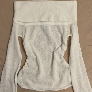 Vit offshoulder stickad tröja - Vit stickad tröja med bred offshoulder-krage och lång ärm. Tröjan har en snygg ribbad struktur och är figurnära med fina detaljer längs sidorna. Perfekt för dig som gillar en stilren och trendig look.