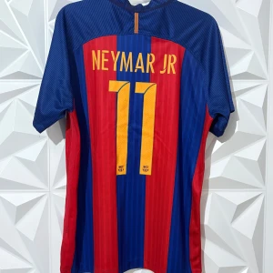 FC Barcelona Neymar Jr 11 matchtröja - Säljer en officiell FC Barcelona matchtröja från Nike med Neymar Jr och nummer 11 på ryggen. Tröjan är blå och röd med gula detaljer, klubbmärke på bröstet och Qatar Airways som sponsor. Tillverkad i lätt och ventilerande material, perfekt för fotbollsfans.